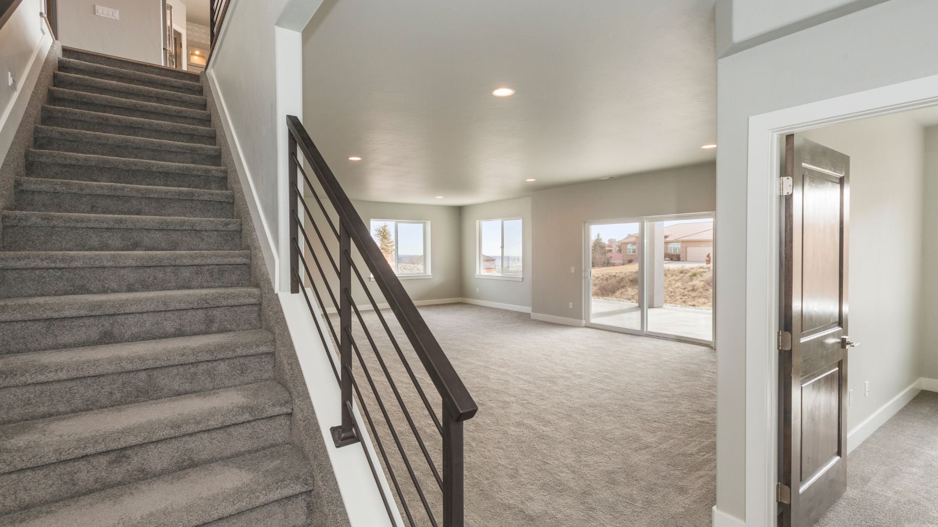 Empty interior with carpeted stairs, modern railing, and large windows