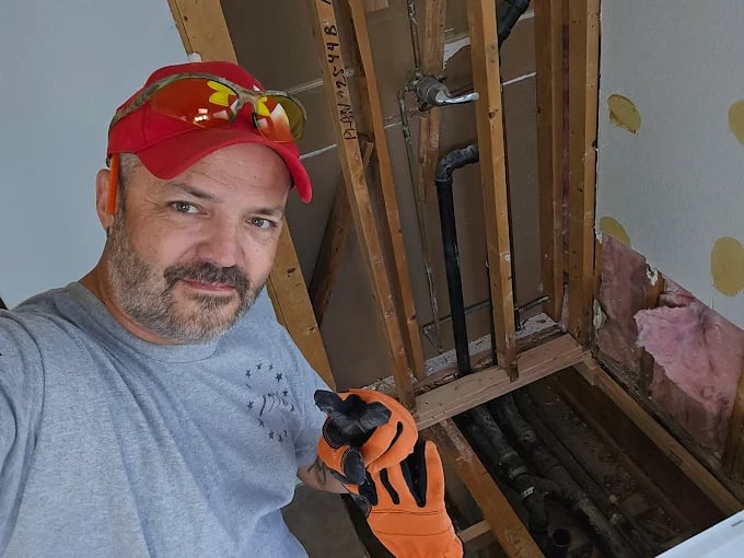 Construction worker wearing red cap and orange gloves inspecting wall framing