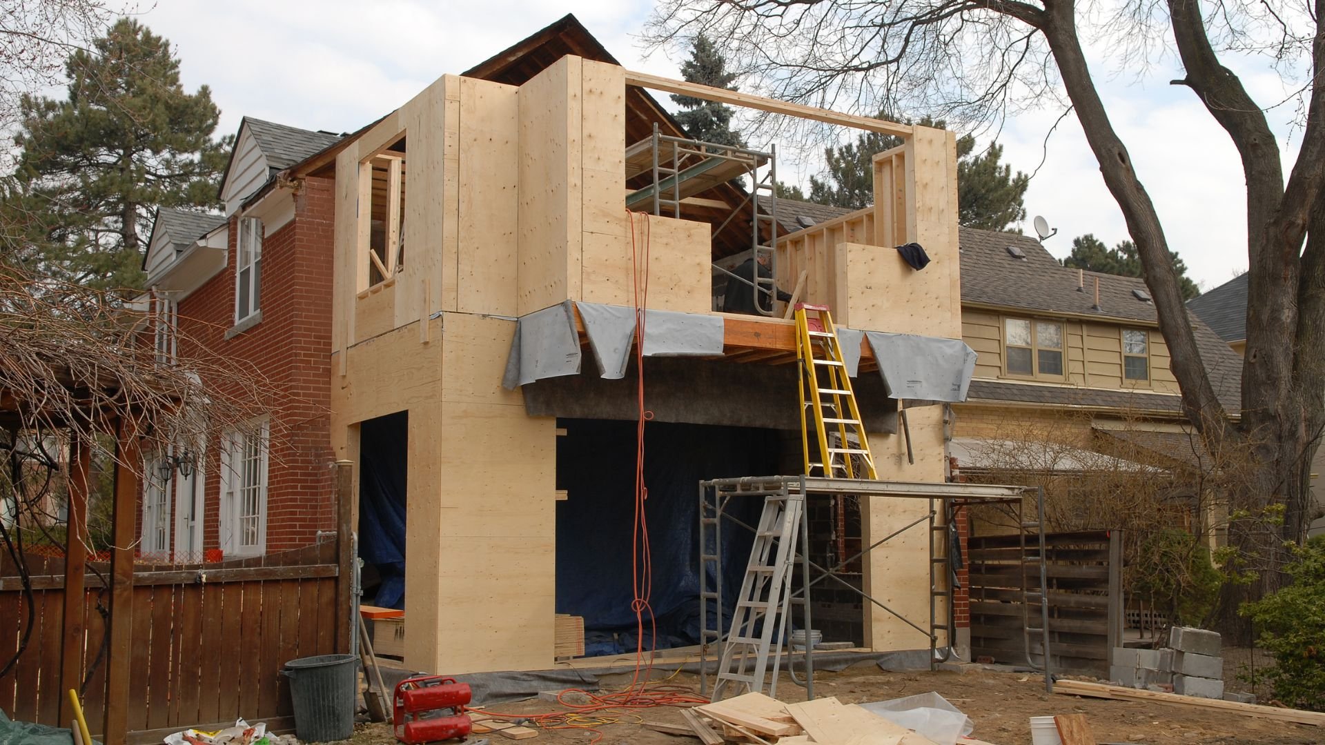 Two-story home addition under construction with wooden framing and scaffolding