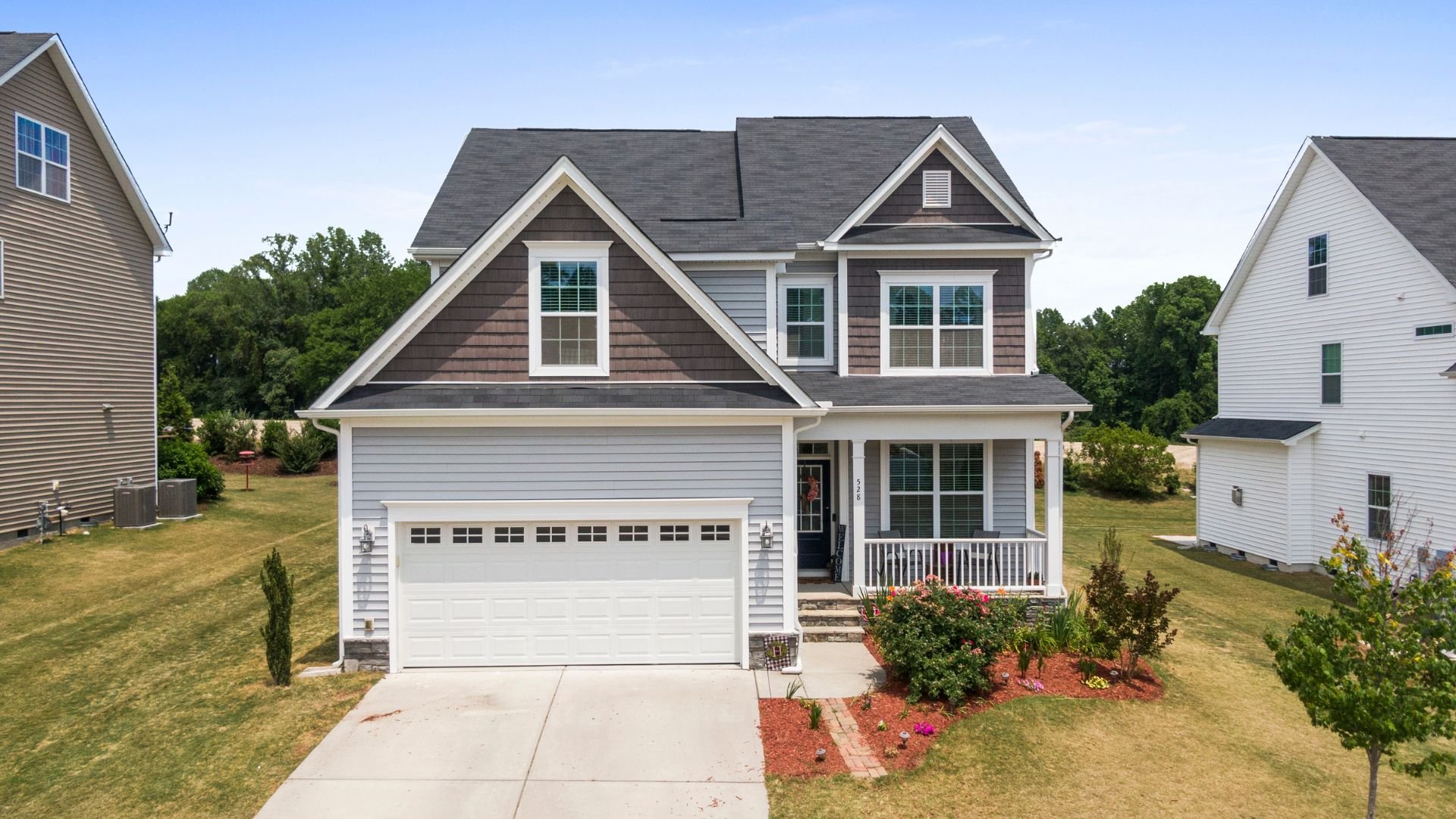 Two-story suburban house with white garage, front porch, and landscaped yard