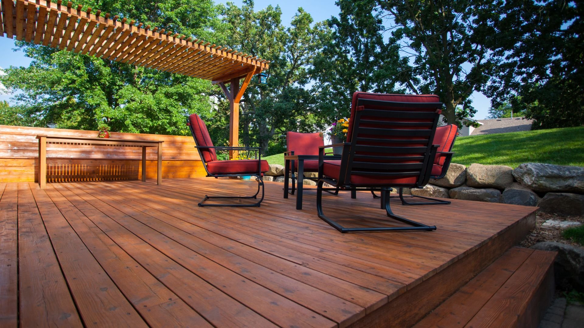 Wooden deck with red chairs, pergola, and trees on a sunny day