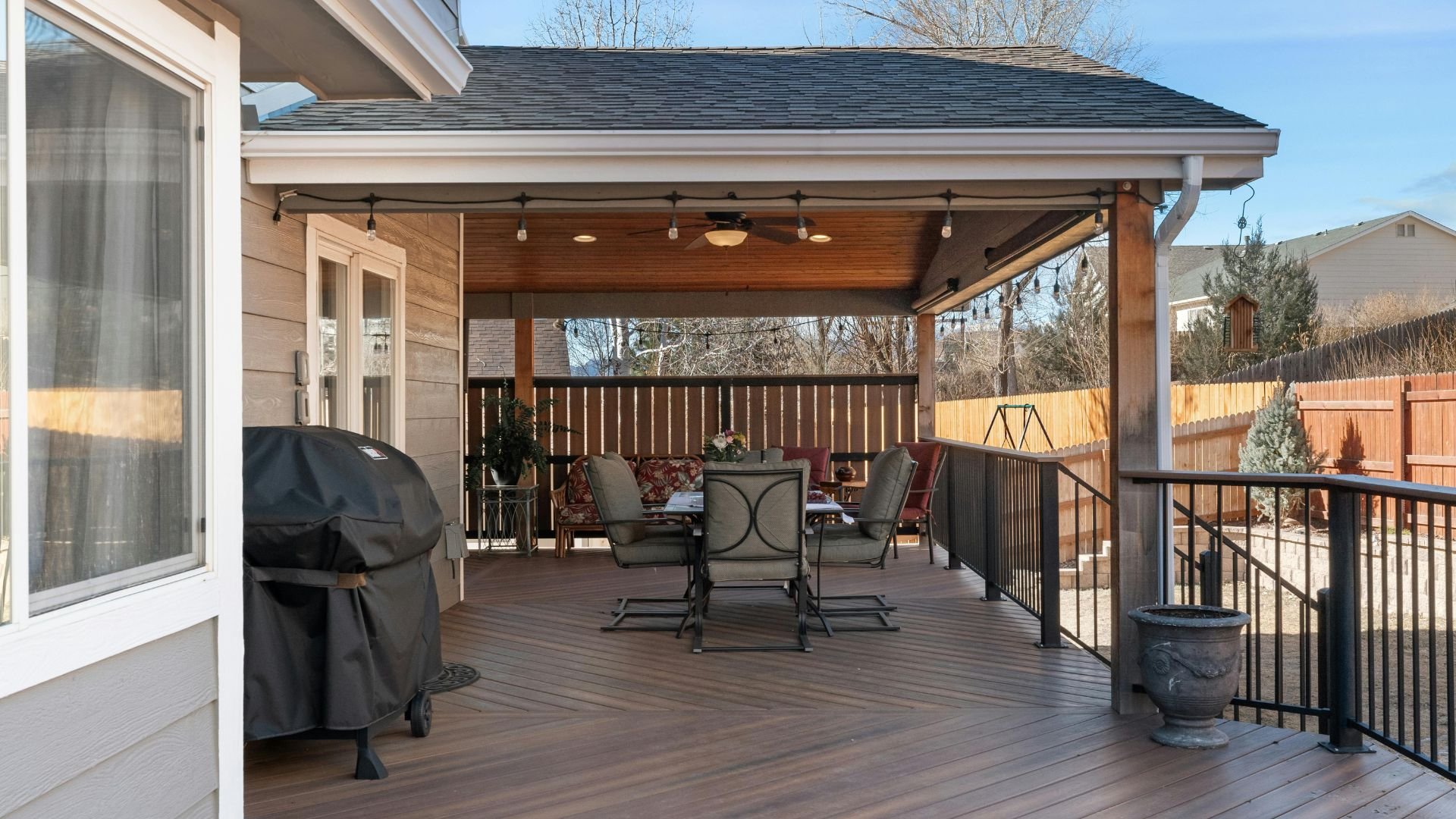 Covered wooden deck with patio furniture, grill, and string lights